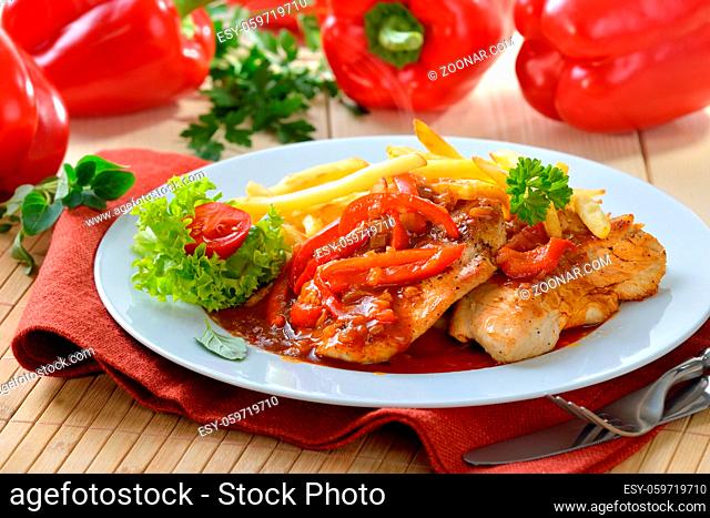 Deftiges Zigeunerschnitzel mit Pommes Frites vor roten Paprikaschoten - Hot escalope with red pepper sauce and French fries
