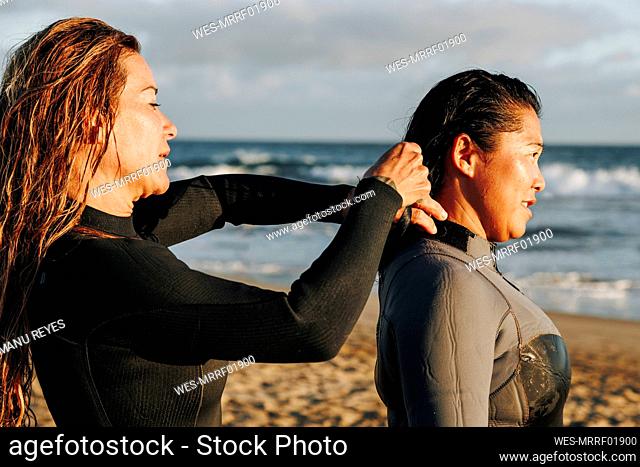 Woman assisting surfer putting on wetsuit at beach, Gran Canaria, Canary Islands