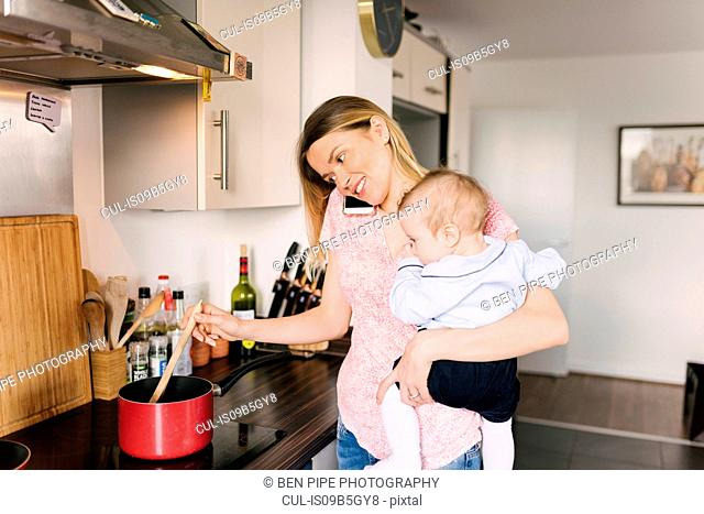 Mother cooking, using telephone and carrying baby in arms
