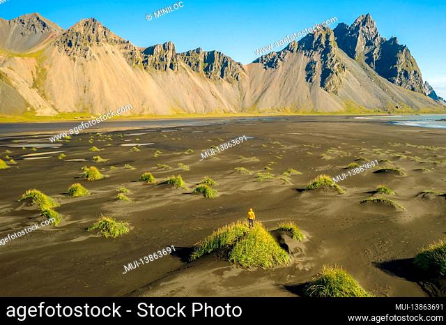 Iceland. Aerial view of man hiker with backpack at black sand dunes on the Stokksnes headland on southeastern Icelandic coast with Vestrahorn. Europe