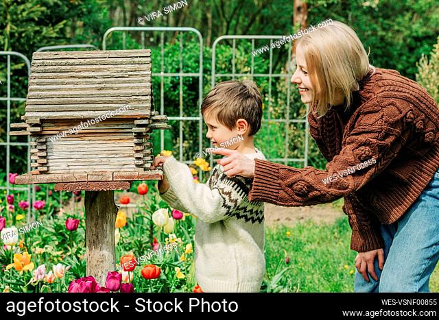 Curious son looking inside birdhouse by mother in garden