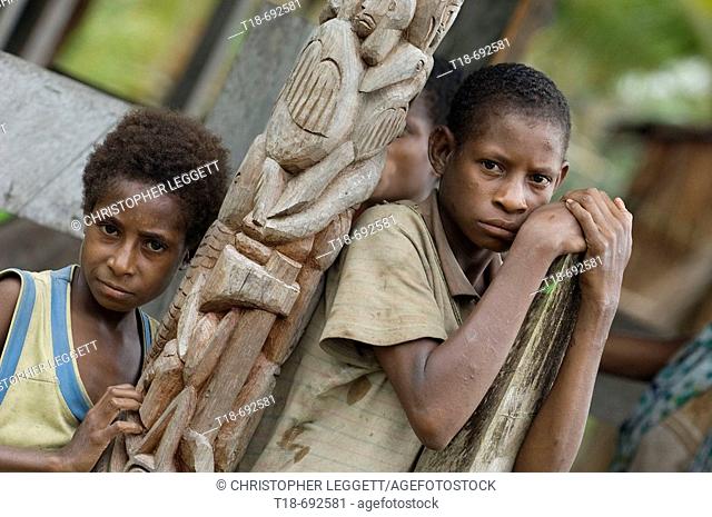 Two boys with disappointed look standing beside wood carving, Indonesia