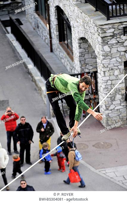 man on a highline slackline over an alley loosing balance, France, Savoie, Val-d?Is?re
