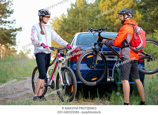 Young Couple Preparing for Riding the Mountain Bikes in the Forest. Unmounting the Bike from Bike Rack on the Car. Adventure and Family Travel Concept