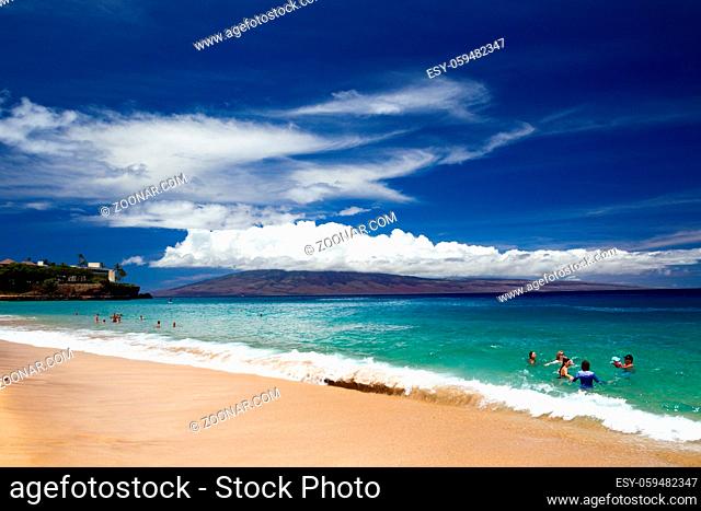 Touristen baden am Strand von Kaanapali Beach auf Maui mit Blick über das Meer auf die benachbarte Insel Lanai in Hawaii, USA