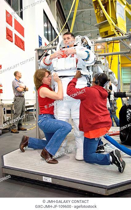 Astronauts Robert S. (Shane) Kimbrough, STS-126 mission specialist, gets help donning a training version of the Extravehicular Mobility Unit (EMU) spacesuit...
