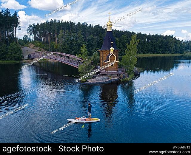 Russia, Leningrad Oblast, Aerial view of paddleboarder passing Church of Saint Andrew at Vuoksa