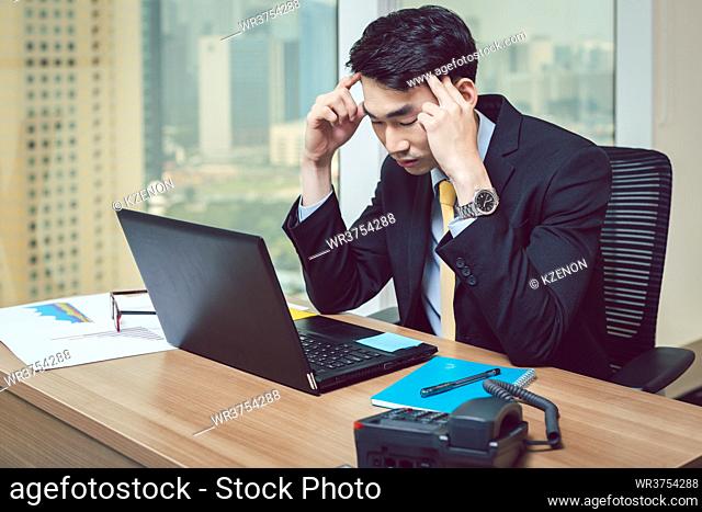 Worried young businessman having headache at workplace