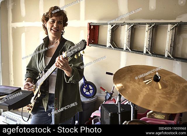 Portrait of guitar player in Garage band composed of middle aged women, practicing in residential garage