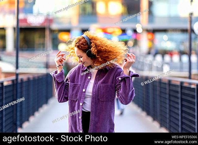 Woman wearing headphones dancing on bridge