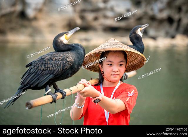 Guilin, China - August 2019 : Cute little chinese girl holding bamboo stick with cormorant birds and posing for souvenir photo in front of the landmark Elephant...
