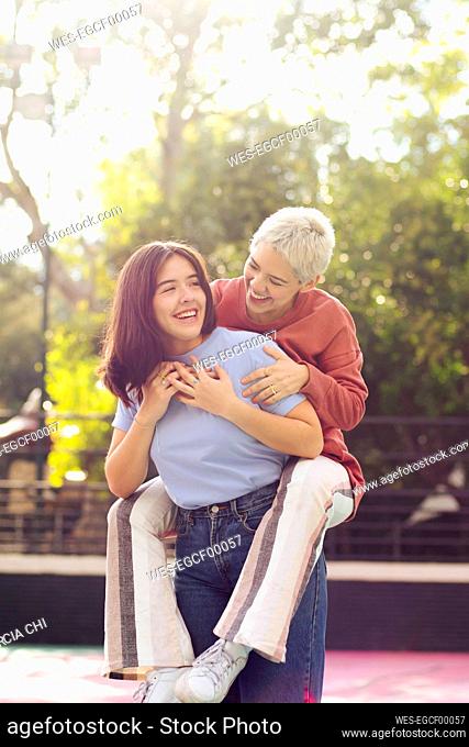 Happy young woman giving piggyback ride to friend on sunny day