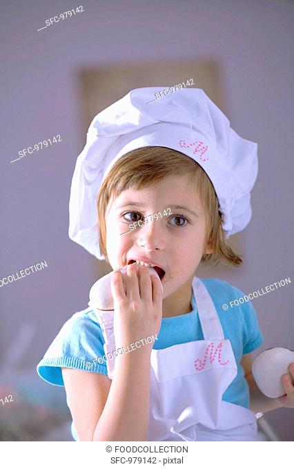 Little girl in chef's hat eating gingerbread