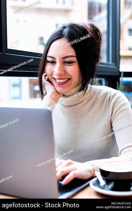 Smiling businesswoman using laptop sitting in cafe