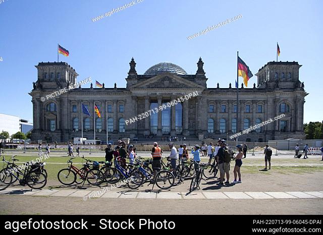 12 July 2022, Berlin: Tourists stand with rental bikes on the lawn in front of the Reichstag. Photo: Paul Zinken/dpa. - Berlin/Berlin/Germany