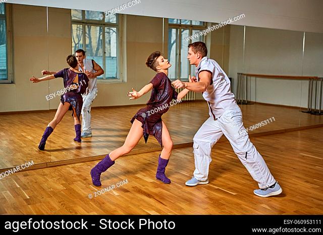 beautiful young couple dancing bachata in dance studio mirror room. woman in purple dress and man in white suit. copy space
