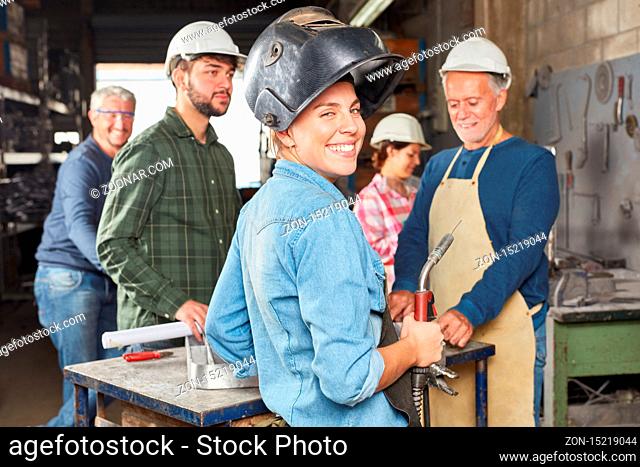 Lächelnde junge Frau als Schweißer im Team einer Schlosser Werkstatt