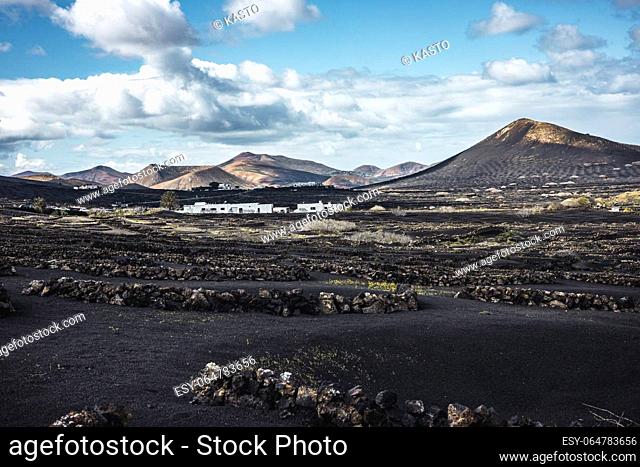 Traditional white houses in black volcanic landscape of La Geria wine growing region with view of Timanfaya National Park in Lanzarote