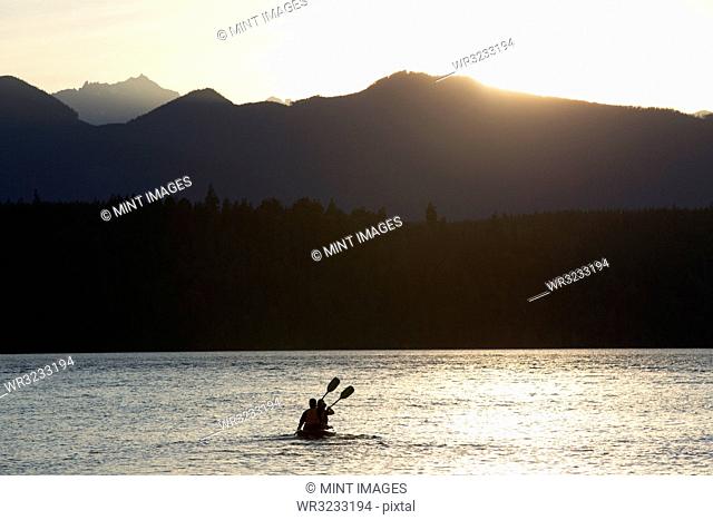 A couple sitting in a sit-on- top Kayak paddling in Puget Sound near the Olympic Mountains in Washington State, USA