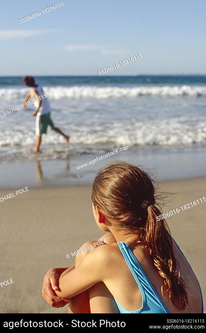 Young girl watching brother throwing shells in the ocean