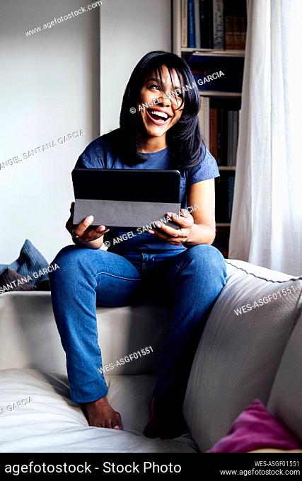 Cheerful woman with digital tablet sitting on sofa at home
