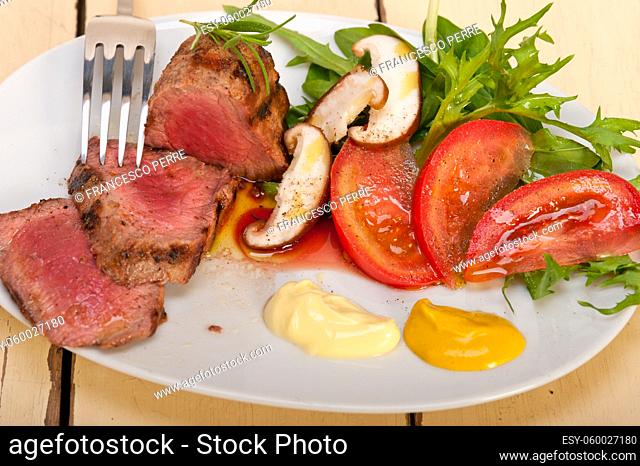 beef filet mignon grilled with fresh vegetables on side , mushrooms tomato and arugula salad
