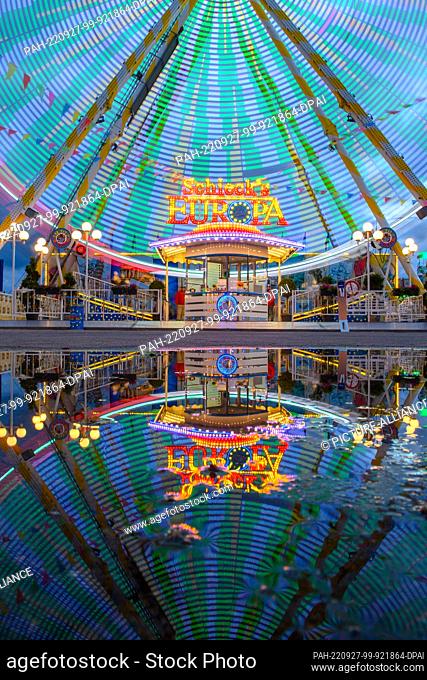 27 September 2022, Saxony-Anhalt, Magdeburg: The Ferris wheel of the Autumn Fair 2022 turns and is reflected in the evening in a rain puddle