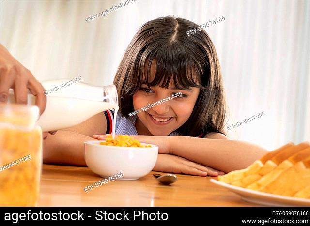 A YOUNG GIRL HAPPILY WAITING TO EAT CORNFLAKES WITH MILK