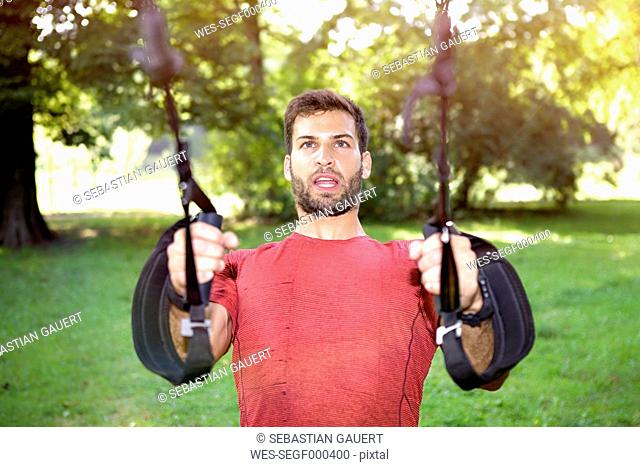 Portrait of sportive man doing TRX training in a park