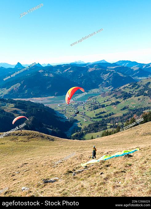Einsiedeln, SZ / Switzerland - November 25, 2018: man with paraglider preparing for take off from a high mountain peak during an instructional course with other...