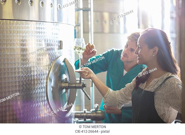 Vintners examining white wine at stainless steel vat in winery cellar
