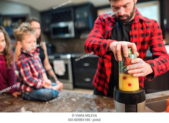 Mother and children watching father blend vegetables in kitchen
