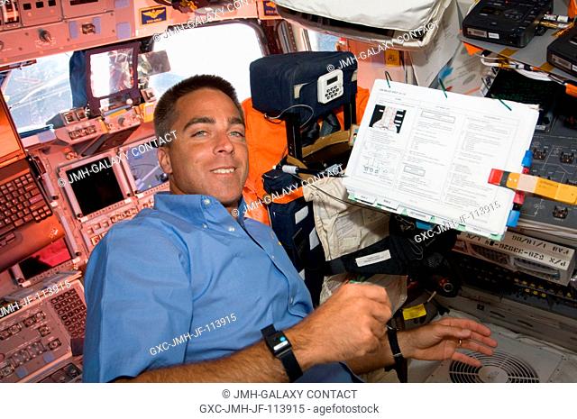 Onboard Endeavour's forward flight deck, astronaut Christopher Cassidy, STS-127 mission specialist, looks over a reference manual as he plays an intravehicular...