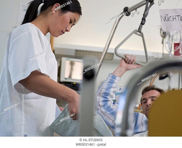 Female nurse changing bed sheet of patients bed