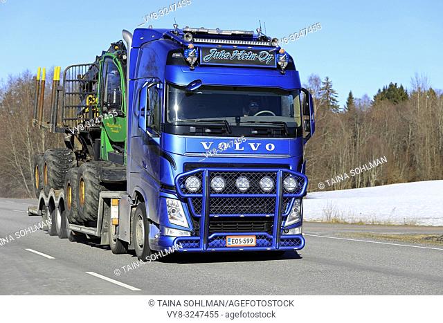 Salo, Finland - February 22, 2018: Blue Volvo FH13 semi truck of Juha Holm Oy hauls John Deere forestry vehicle along highway on a day of winter