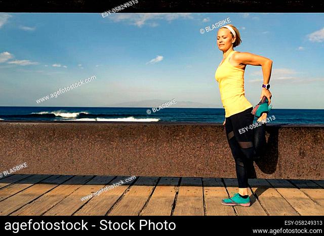 Woman runner stretching at the seaside on sunny summer day. Fitness girl running and exercising on a coastline in Tenerife, Spain