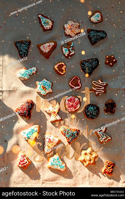 Christmas gingerbread cookies in many shapes decorated with colorful frosting, sprinkle, icing, chocolate coating, toppers, put on plain fabric