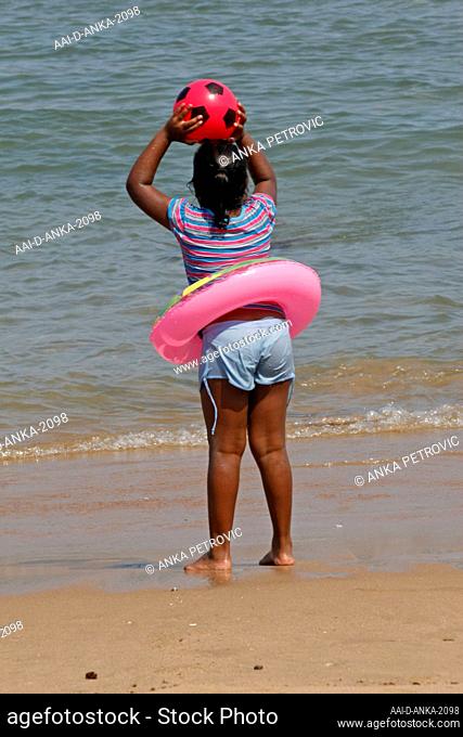 Child on the beach with floating ring throwing pink ball, Umfolozi beach, KwaZulu Natal, South Africa