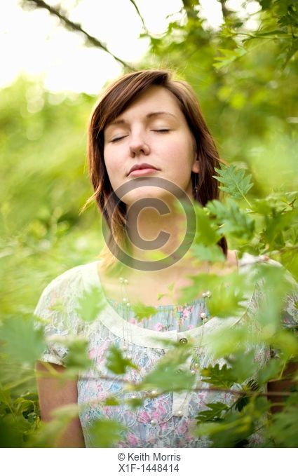 A young slim attractive girl in her late teens or early 20's, outdoors in a woodland glade  with her eyes closed, UK