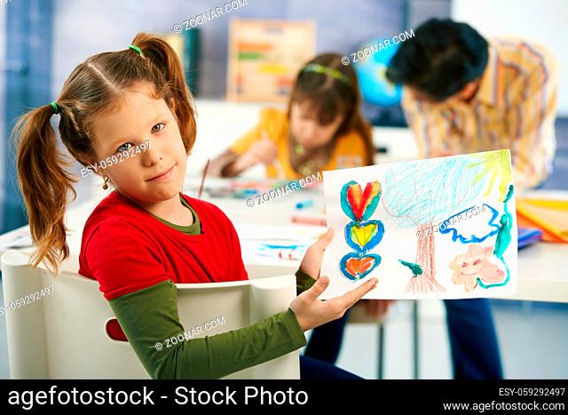Portrait of elementary age schoolgirl showing colorful paining to camera in art class in primary school classroom