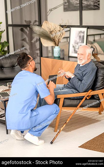 Smiling pleased gray-haired man ticking something off on his fingers during the conversation with his in-home caregiver