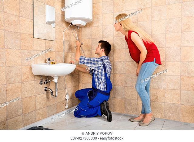 Young Woman Looking At Male Worker Installing Electric Boiler At Bathroom