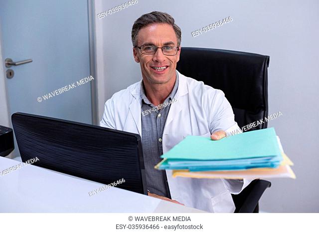 Portrait of dentist holding file while sitting by computer