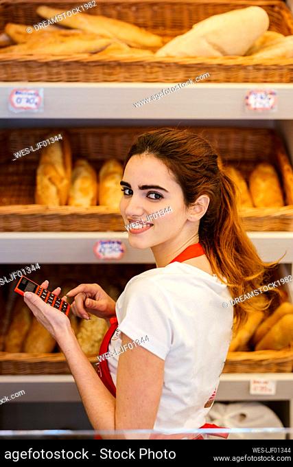 Young woman working in a bakery and using calculator