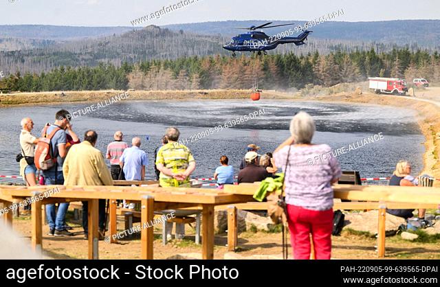 05 September 2022, Lower Saxony, Braunlage: A helicopter of the federal police takes water from a lake on the Wurmberg, while numerous hikers and onlookers...