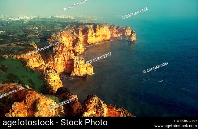 Aerial panoramic image above view of Ponta da Piedade headland with group of rock formations yellow-golden cliffs along limestone coastline, Lagos town