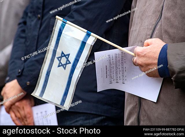 09 November 2023, Mecklenburg-Western Pomerania, Greifswald: A participant in an ecumenical service holds an Israeli flag at the site of the former prayer hall...