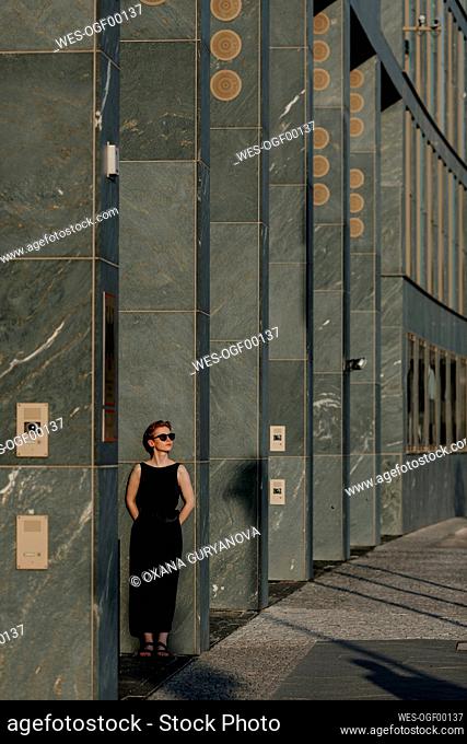 Red-haired woman with sunglasses, leaning on pillars in the city