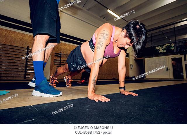 Trainer standing over pregnant woman doing push ups in gym