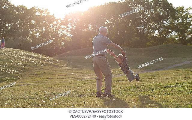 Handsome grandad spinning around toddler boy